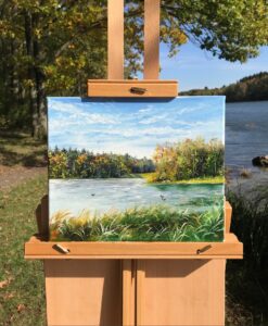 Autumn lake oil painting displayed on a wooden easel beside the water