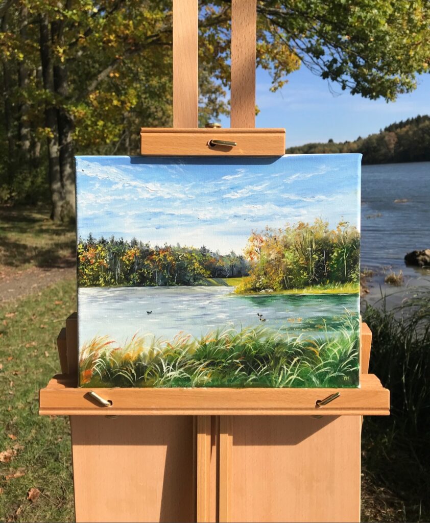 Autumn lake oil painting displayed on a wooden easel beside the water