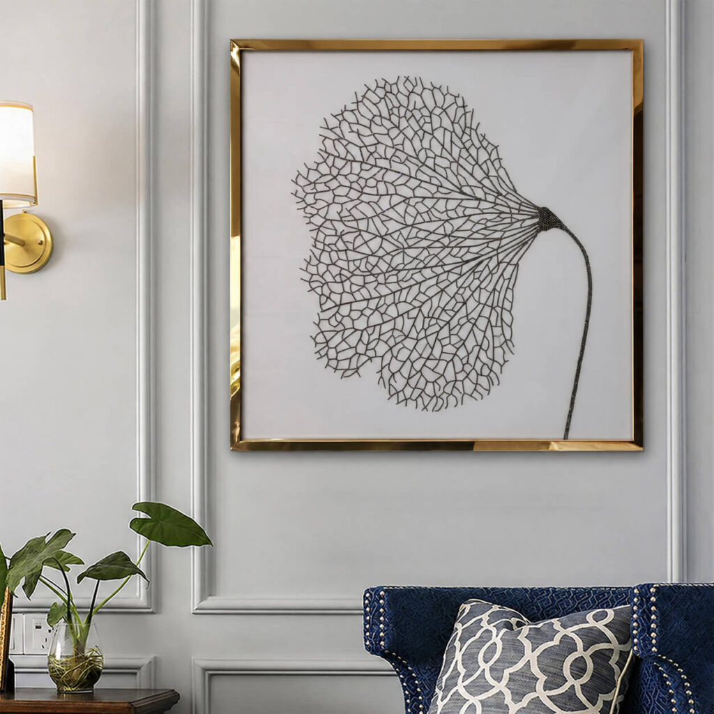 Gold framed black leaf wall art displayed above a blue upholstered chair