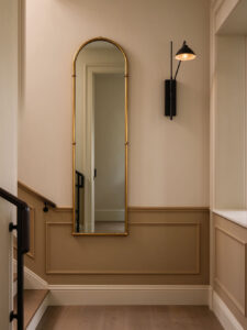 Arched gold mirror with stylish wall sconce on staircase landing